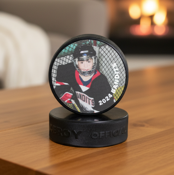 A custom hockey pucks display stand featuring a printed photo of a hockey player on the top puck, resting on a black puck base.  The setup is placed on a wooden table with a blurred living room background.