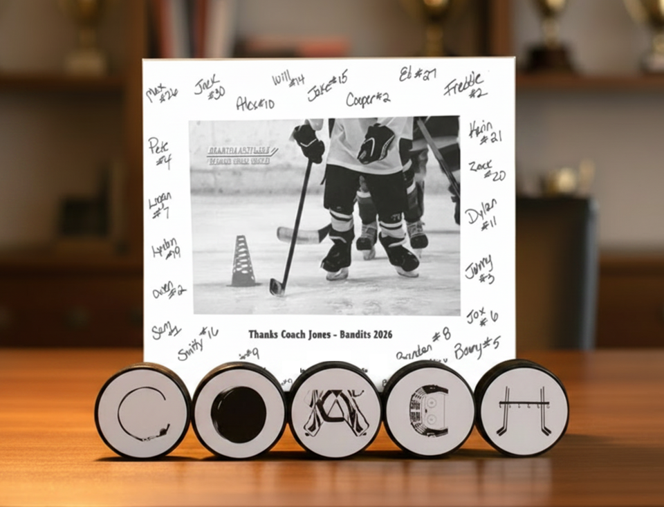 A custom hockey-themed photo plaque displayed on a wooden table, featuring a white background with handwritten player names, a central black-and-white hockey player photo, and a thank-you message.  This is displayed in hockey pucks with COACH spelled out on the the pucks in unique hockey letters.