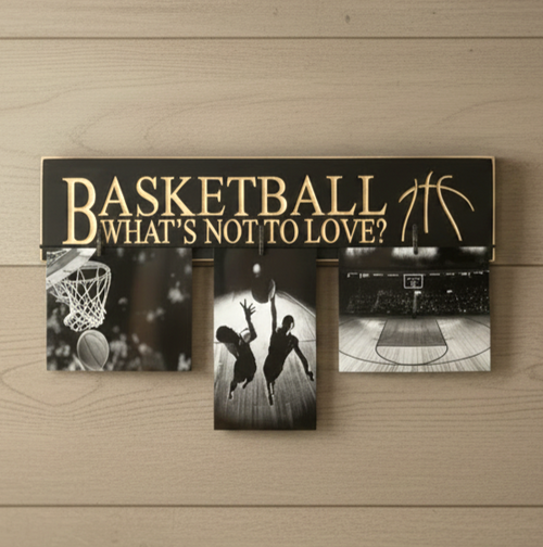 A rectangular black basketball-themed wall sign with carved lettering reading “BASKETBALL WHAT’S NOT TO LOVE?” and gold basketball graphics, mounted on a light wood wall. Three black-and-white basketball photos are clipped or displayed below the sign.