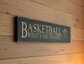 A rectangular black wooden sign with engtraved lettering that reads 'BASKETBALL WHAT'S NOT TO LOVE?' mounted on a light wood plank wall.
