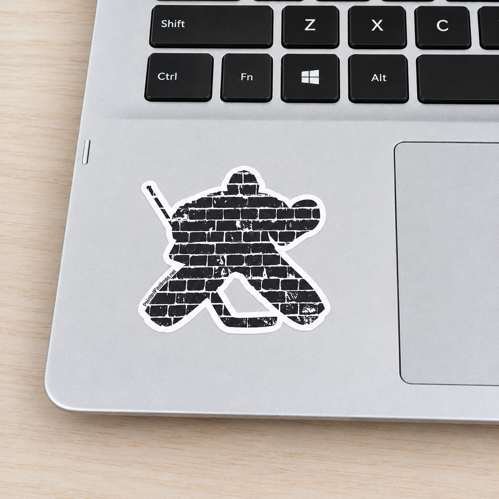 A die-cut vinyl sticker of a hockey goalie silhouette filled with a distressed black brick pattern, shown applied to a silver laptop on a light wood desk.