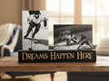 A decorative wooden sign on a table in a living room setting, featuring two black-and-white hockey photographs mounted above the words “DREAMS HAPPEN HERE” in carved lettering.