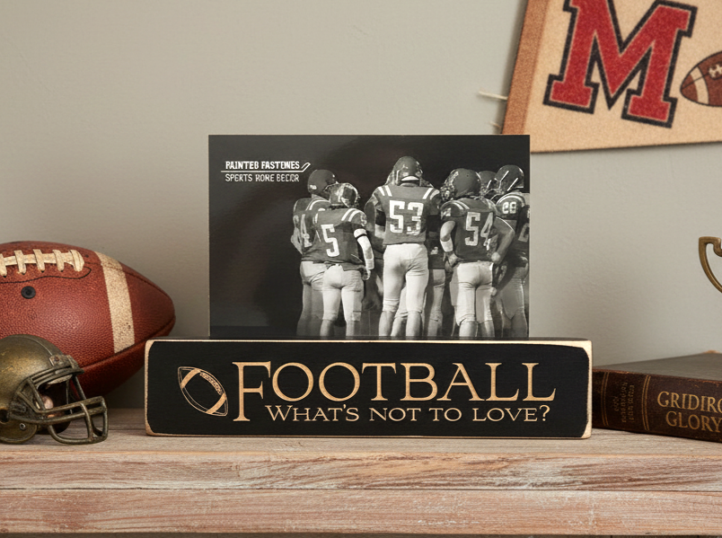 A decorative wooden sign on a tabletop reads “FOOTBALL What’s Not to Love?” with a football graphic and a black-and-white photo of football players behind it. The sign is styled on a shelf with a football, helmet, book, and wall decor in the background.