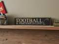A rectangular dark wood sign with carved lettering that reads 'FOOTBALL WHAT'S NOT TO LOVE?' displayed on a rustic wooden shelf next to a football helmet and books.