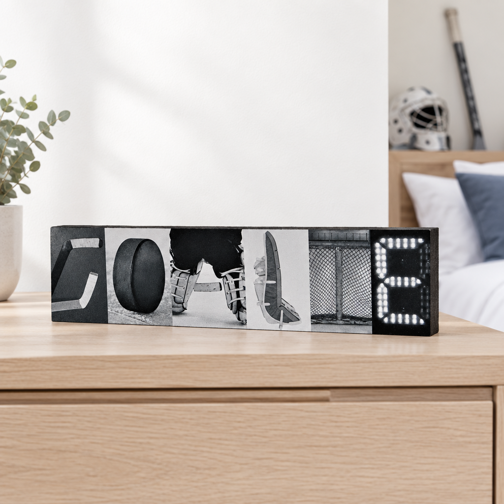 A sign spelling out "GOALIE" in hockey goalie photos, sitting on a light wood dresser in a hockey goalie bedroom setting.