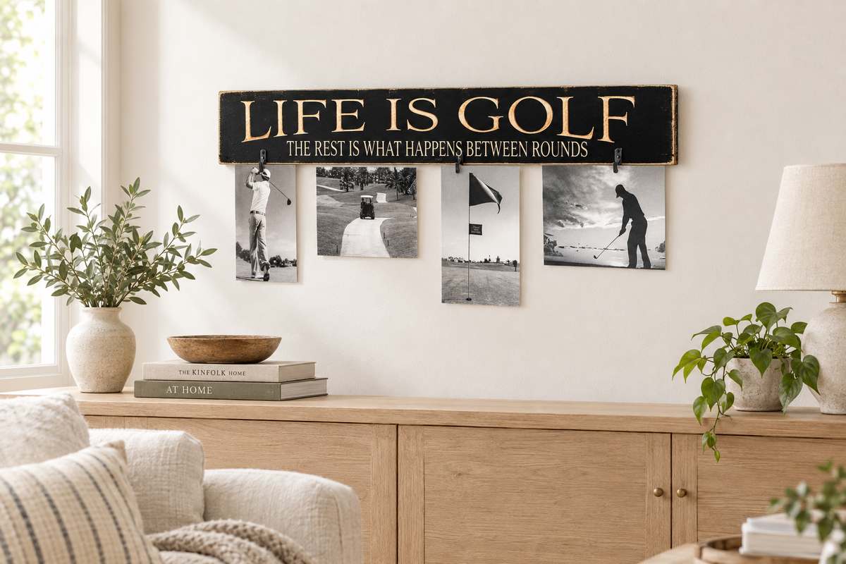 Black wooden sign with engraved lettering that reads "Life is Golf. The rest is what happens between rounds."  Four black and white photos are attached to the sign with clothespins. The photos show a golfer swinging a club, a golf cart on a path, a golf flag, and a golfer putting.