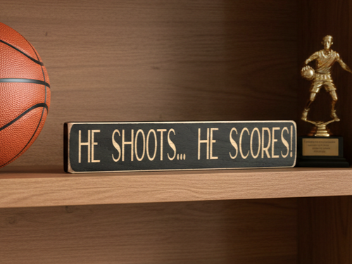 A wooden sign with engraving "He Shoots... He Scores" in a basketball setting shelf