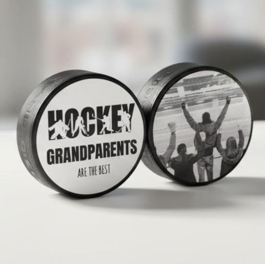 Two connected hockey pucks on a light gray surface. One puck is white with black text reading 'HOCKEY GRANDPARENTS ARE THE BEST' and silhouettes of players.  The other puck has a hockey photo on it.