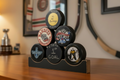 A set of six custom hockey pucks stacked on a black wooden display stand on a wooden table, with a blurred hockey room background.