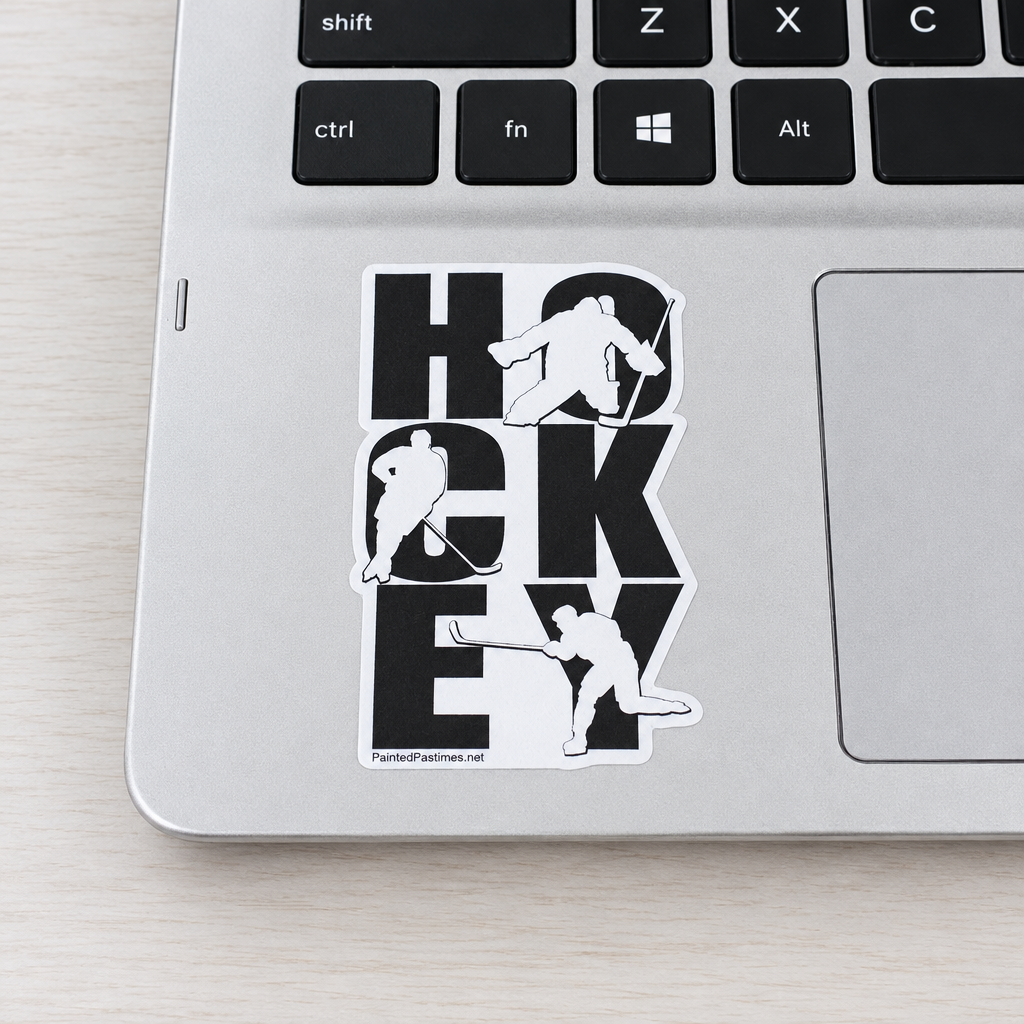 A die-cut vinyl sticker featuring the word 'HOCKEY' in bold black letters with white hockey player silhouettes, shown applied to a silver laptop on a light wood surface.