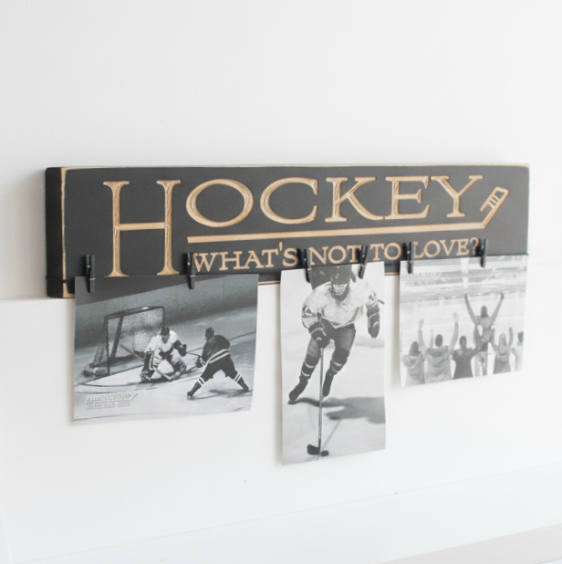 A black wooden hockey-themed wall sign with the word 'HOCKEY' in large endgraved letters and "What's not to love?" and clips holding three black-and-white hockey photos against a white wall.