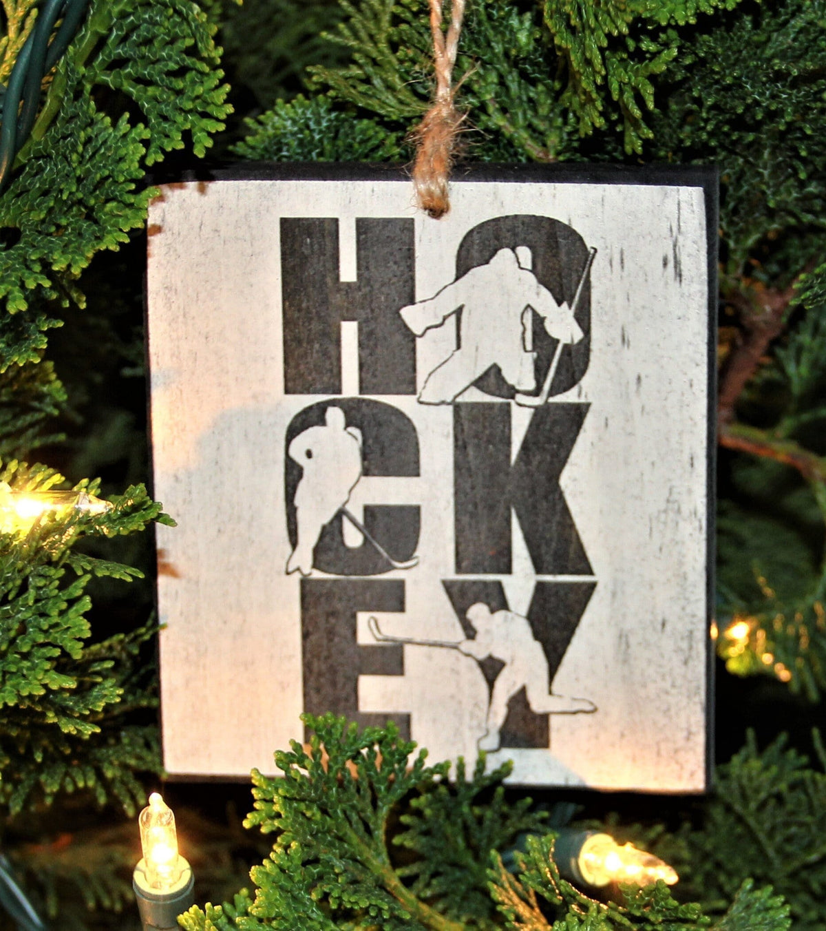 May include: A white wooden ornament with black text and silhouettes of hockey players. The text reads "HOCKEY"