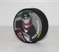 Hockey puck with a photo of a hockey player and the name of the team and year, sitting on a white table and white shiplap background.