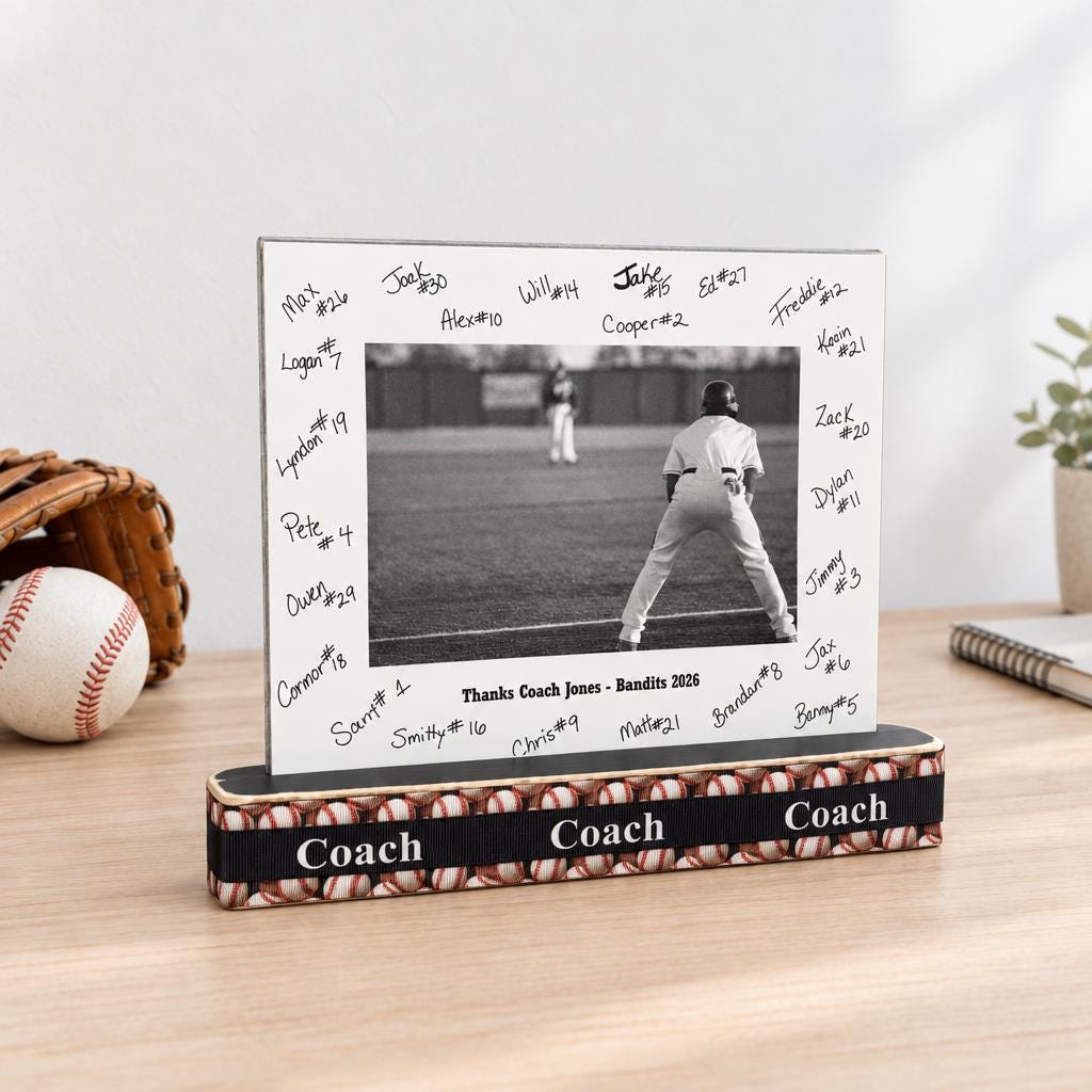 A baseball coach photo frame with a wooden base with baseballs and COACH and a matted baseball photo  with the team signatures all on the mat and custom team name and year as well.  This sits on a natural wooden desk along with a baseball, glove and a plant.