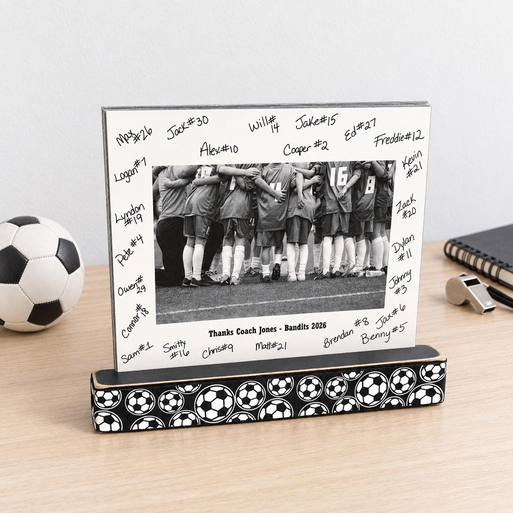A soccer photo display with a wooden base with soccer balls and a matted photo of a soccer team with the team signatures all on the mat and custom team name and year as well.  This sits on a natural wooden desk along with a soccer ball, whistle and book.