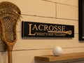 Wood sign with carved text "Lacrosse What's not to love?"  and a lacroose stick set in a room with lacrosse decor 