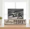 A decorative wooden hockey sign on a tabletop with a black-and-white hockey photo leaning on top. The sign reads “Life is better with HOCKEY” and includes small player silhouettes.