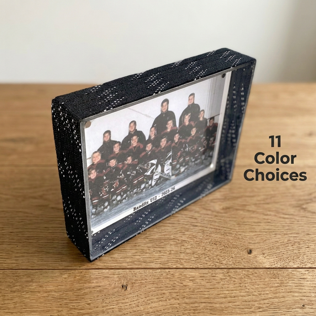 A rectangular black hockey laces photo frame with a team photograph inside, placed on a wooden tabletop against a light wall. Text on the right reads '11 Color Choices'.