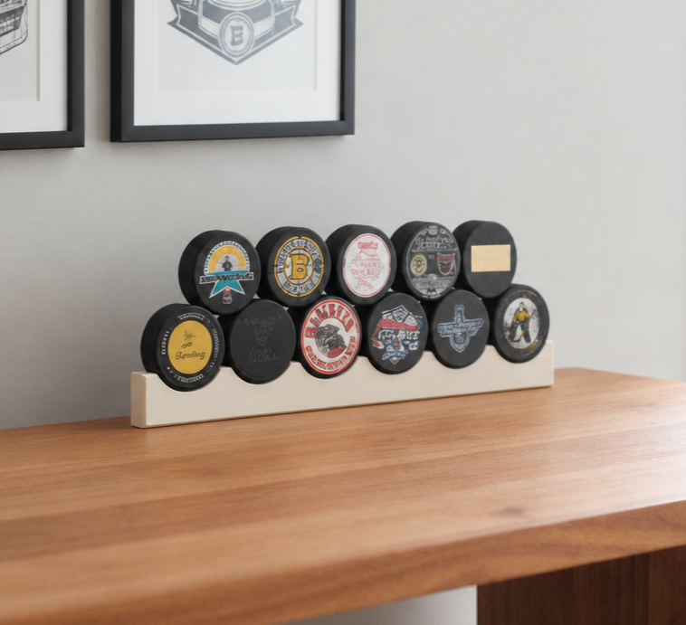 A set of hockey pucks arranged on a white wooden display stand placed on a wooden table, with framed wall art in the background.