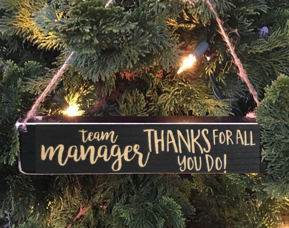 Decorative sign hanging on a Christmas tree with 'Team Manager Thanks for All You Do!' text.