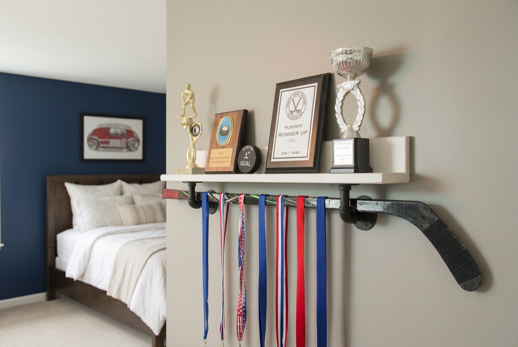 A wall-mounted hockey-themed trophy shelf in a bedroom setting, holding framed awards, a silver cup, and hockey stick below with several hanging sports ribbons.